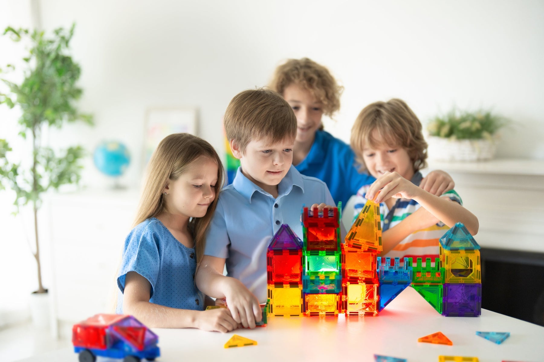 Vier Kinder konstruieren gemeinsam mit Magneo Magnetbausteinen ein farbenfrohes Bauwerk. Teamwork, Kreativität und STEM-Lernen im MontessoriZuhause.